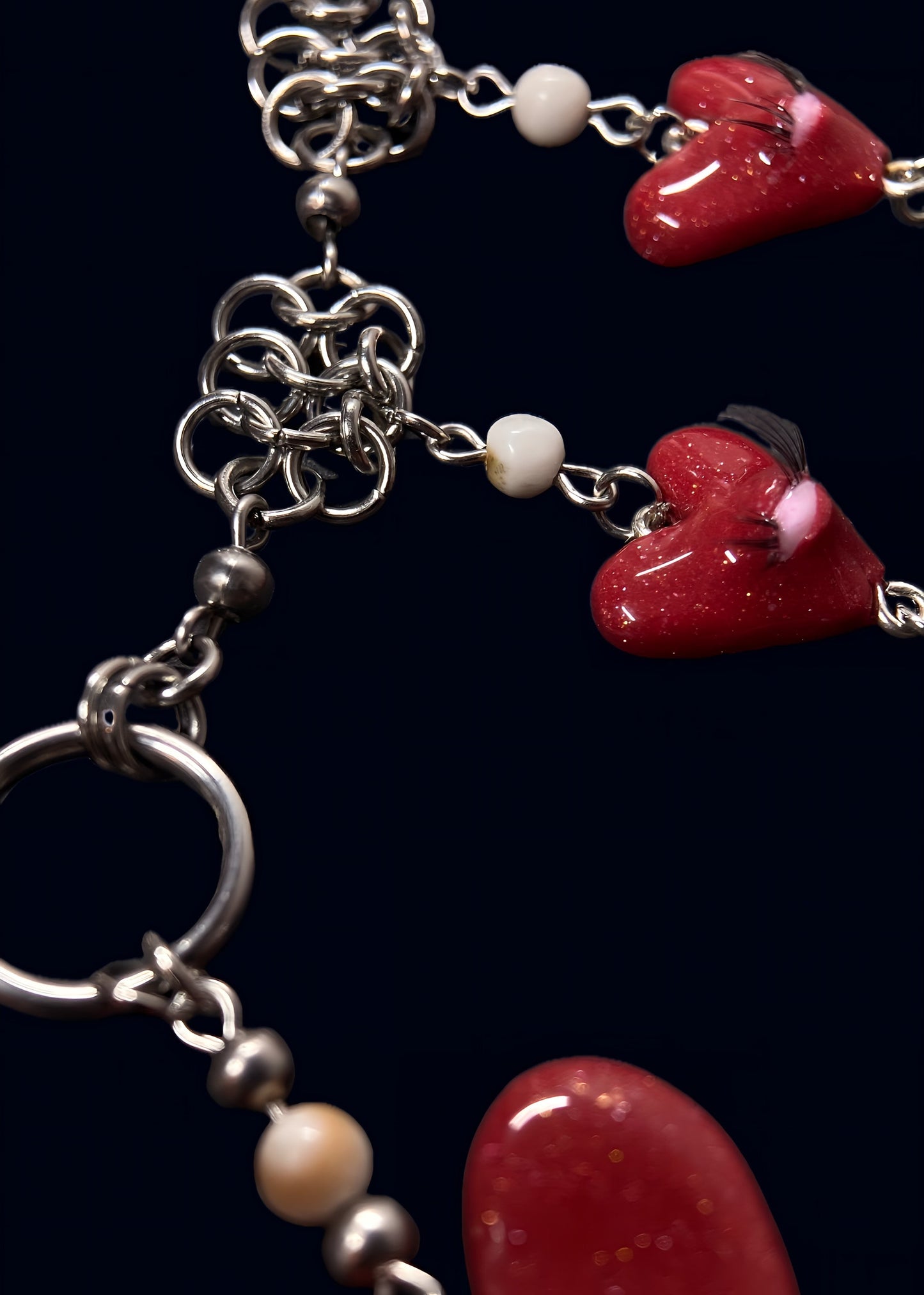 close up product photo of chainmail and pearl part from handmade glittery heart swarm necklace. small red heart pendant with one pink eye and small lashes, thrifted red and white pearls dangling from the heart and chainmail necklace. more of the necklace out of focus.