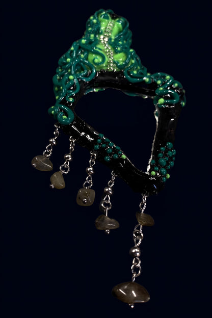 angled front view of green alien mirror showing sculpted tentacle details and hanging stone chain drops against dark blue backdrop