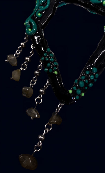 close-up of silver stainless steel chains with stone chip drops hanging from black mirror frame, green bead accents visible