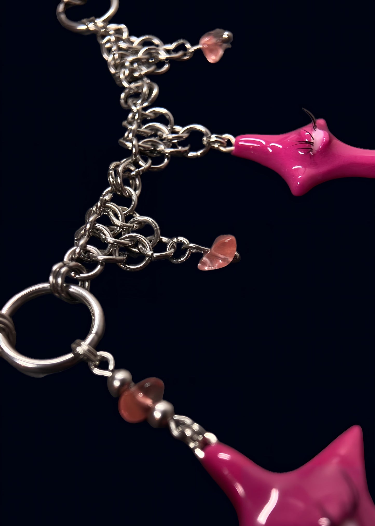 macro close-up of glossy pink star pendant with raised eye detail and reflective resin surface, chainmail and rose quartz beads partially visible