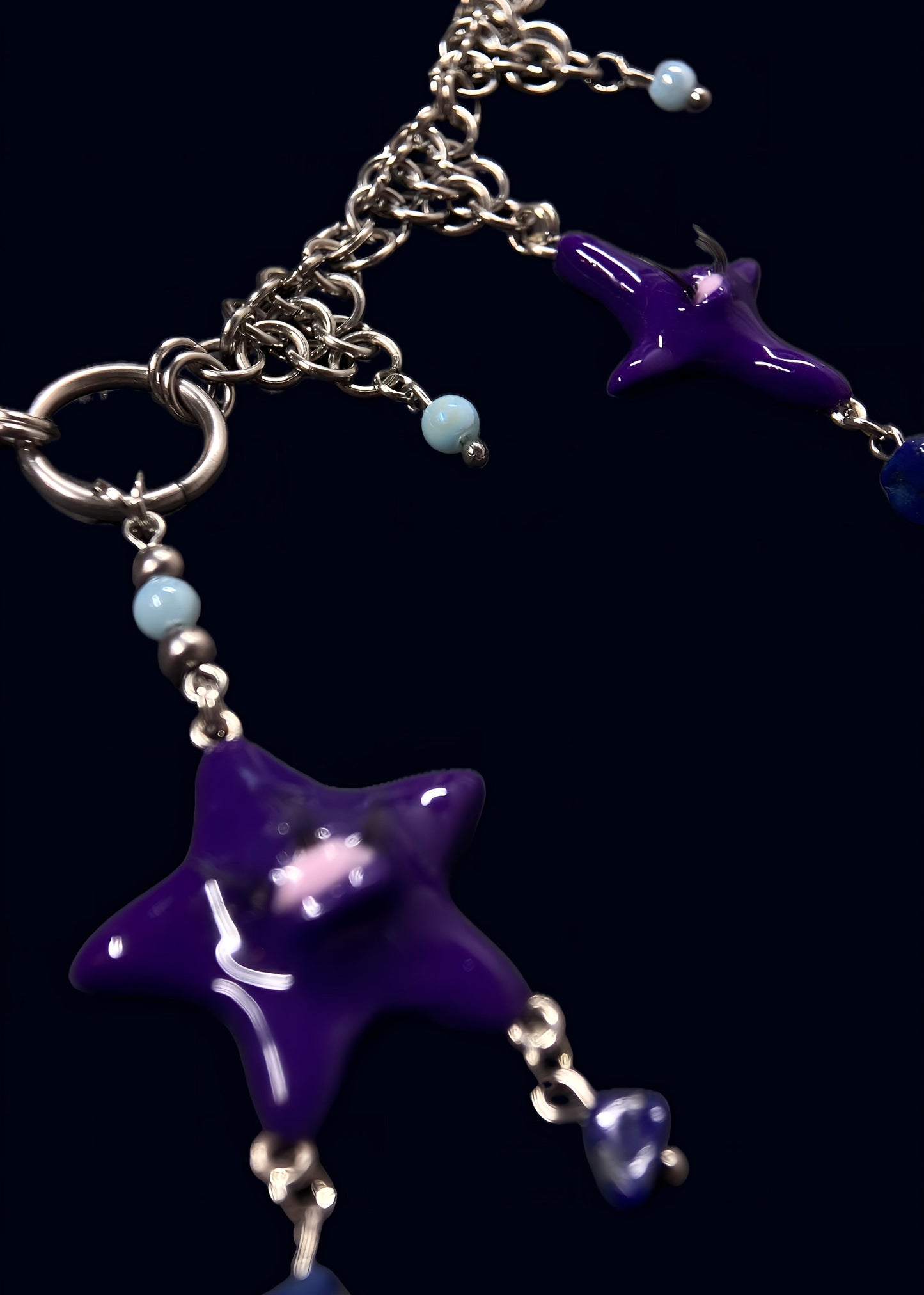 angled close-up of purple star pendant connected to large metal ring, showing chainmail structure and light blue bead drops