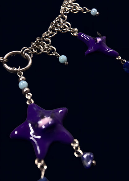 angled close-up of purple star pendant connected to large metal ring, showing chainmail structure and light blue bead drops