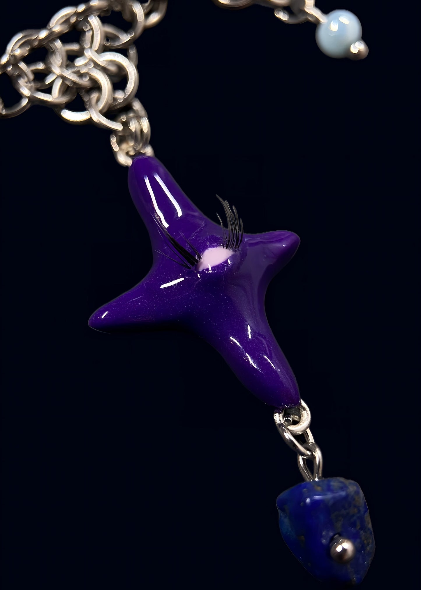 macro detail of glossy purple star pendant with raised eye and fine lashes, deep reflective resin surface