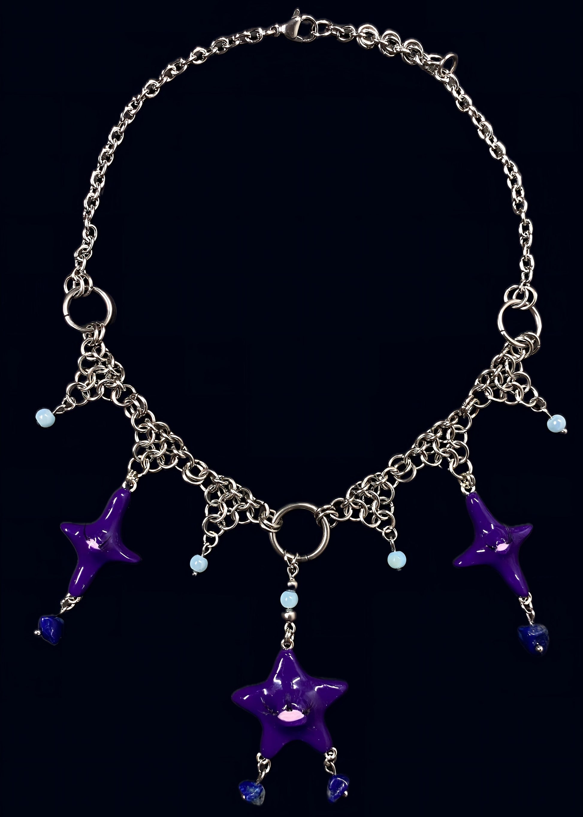 full view of purple gazing star necklace laid flat on dark blue background, central purple eye star pendant with multiple dangling stone drops and symmetrical chain arrangement