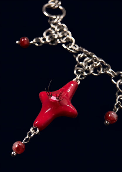 detail photo of red heart creature necklace showing layered stainless steel chainmail, red bead accents and glossy red star charm