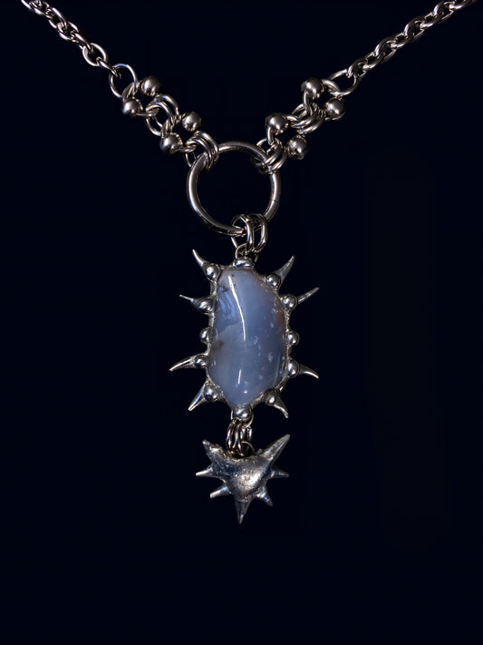 product photo of blue chalcedony gemstone held inside a hand-formed spiked frame made with soft solder. hanging from big o-ring attached to stainless steel link chain. 