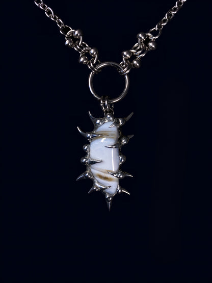 product photo of white calcite gemstone held inside a hand-formed spiked frame made with soft solder. soft brown stripes on the stone. hanging from big o-ring attached to stainless steel link chain. 