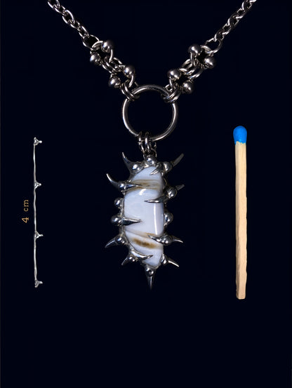 product photo of white calcite gemstone held inside a hand-formed spiked frame made with soft solder. soft brown stripes on the stone. hanging from big o-ring attached to stainless steel link chain. next to it a match to compare size and a measurement of 4 cm. 
