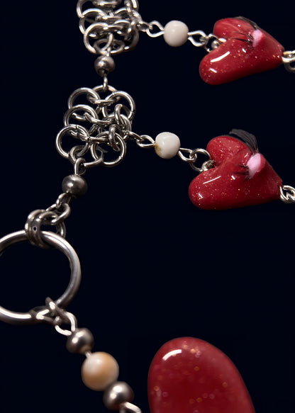 close up product photo of chainmail and pearl part from handmade glittery heart swarm necklace. small red heart pendant with one pink eye and small lashes, thrifted red and white pearls dangling from the heart and chainmail necklace. more of the necklace out of focus. 