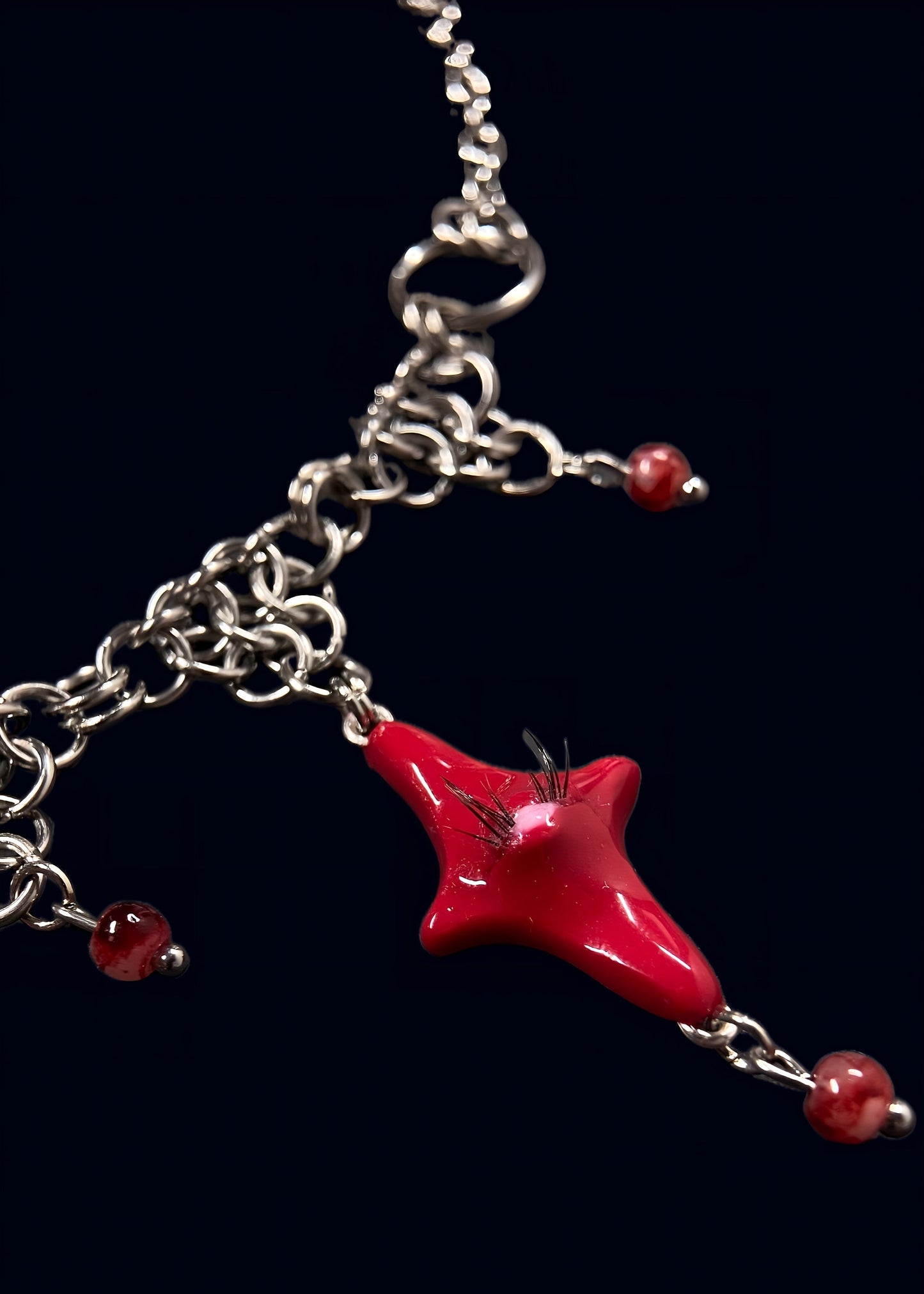 close up product photo of the smaller star pendant. focus on small red star pendant with one pink eye and small lashes, thrifted red pearls dangling from the heart and chainmail necklace. 