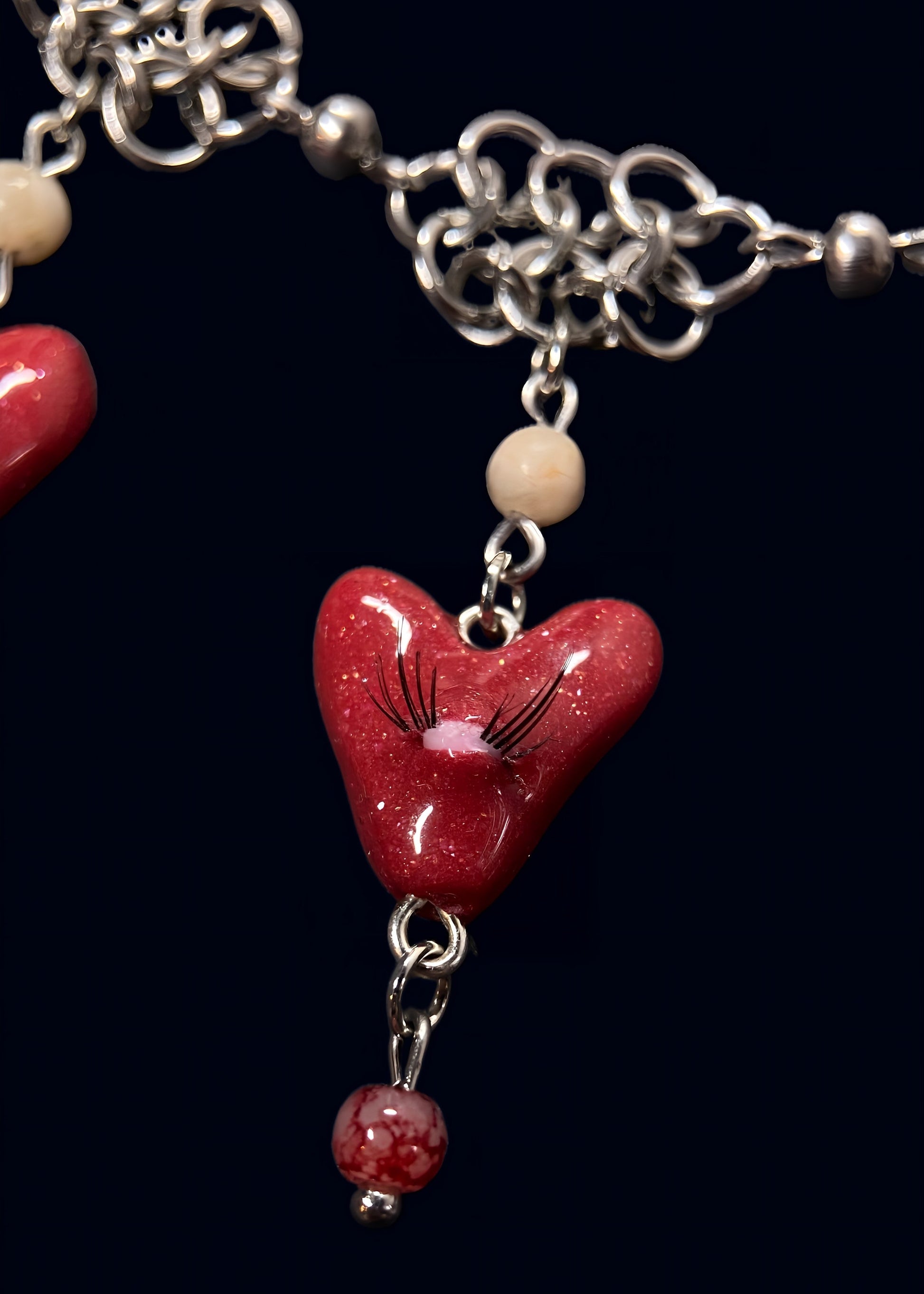 close up product photo of other small pendant from handmade glittery heart swarm necklace. small red heart pendant with one pink eye and small lashes, thrifted red and white pearls dangling from the heart and chainmail necklace. 