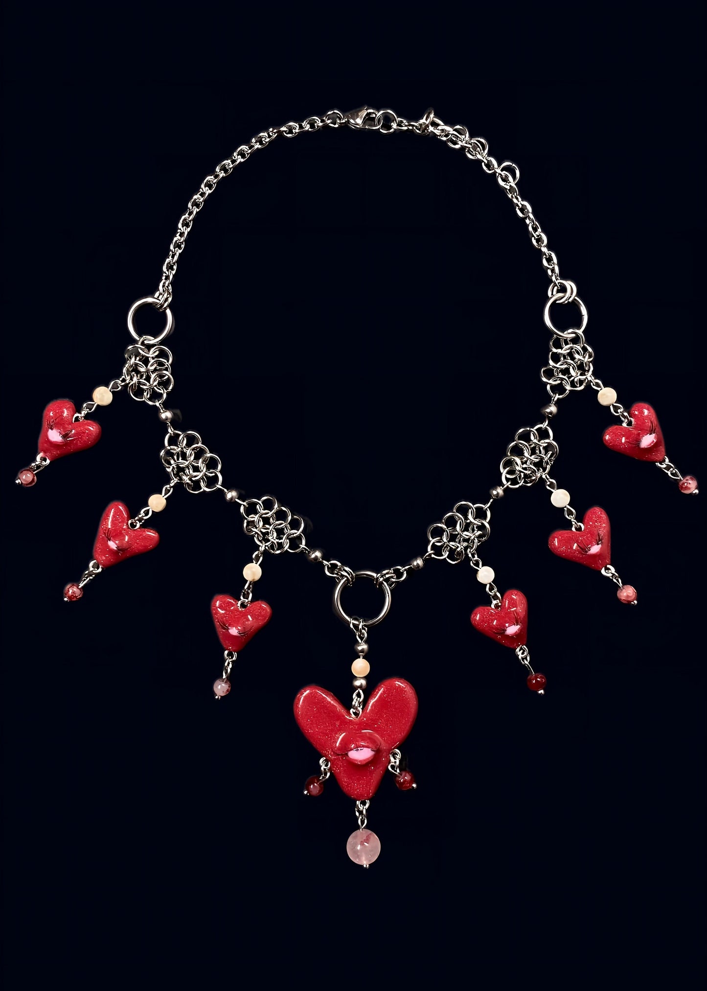 handmade glittery red polymer clay heart swarm necklace: central large red heart pendant with one eye and lashes, six smaller red glitter hearts clustered around it, thrifted red and white pearls dangling from each heart and woven into stainless steel chainmail necklace, glossy uv resin finish, queer fairycore alt-fashion jewelry by softedgez from berlin