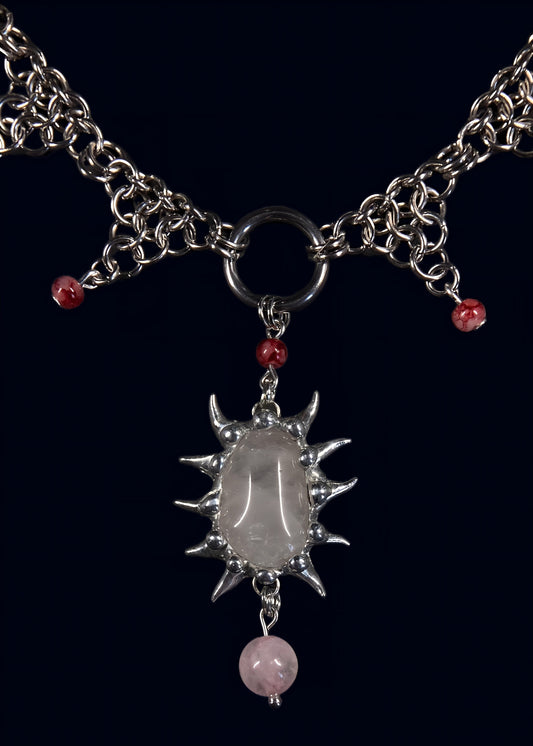 close-up of rose quartz held in hand-built spiked soft solder frame attached to large o-ring and stainless steel chain with small red accent beads