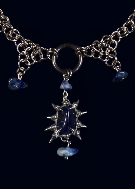 close-up of deep blue sodalite stone framed by jagged soft solder spikes hanging from round o-ring on stainless steel chain